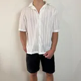 Camisa de manga corta confeccionada en tejido de crochet con diseño de rayas verticales, cuello solapa y cierre frontal con botones.
