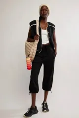 Chaleco de tejido tipo corderito color negro, con cierre frontal de botones a presión y bordes en color beige. Presenta un diseño sin mangas con corte recto.