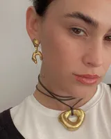 Collar con dije de forma irregular en tonos dorados y plateados, suspendido de un cordón doble de algodón negro.