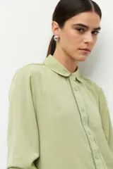 Camisa verde claro de manga larga con cuello clásico y cierre frontal con botones. Presenta detalles de vainillas en puños y frente.