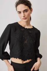 Blusa negra con detalles de apliques bordados en el pecho y las mangas, cuello redondo y mangas largas abullonadas.