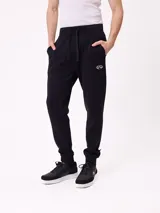 Babucha jogger color gris oscuro, con cintura elástica ajustable con cordón, bolsillos laterales y puños elásticos en los tobillos. Presenta un logo estampado en el muslo izquierdo.