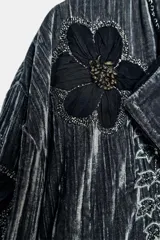 Kimono de terciopelo gris con acabado texturizado, cuello redondo y manga larga. Presenta bordados florales en hilo negro y metalizado, bolsillos delanteros y cierre frontal.
