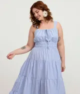 Vestido midi de Ashua confeccionado en tricolina de algodón, con diseño a rayas celestes y blancas. Presenta escote cuadrado con cordón ajustable fruncido, tiras anchas, cintura elástica y falda escalonada con volados.