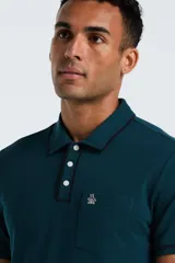 Chomba de piqué color verde petróleo, con cuello clásico, cierre frontal de tres botones y bolsillo frontal con logo bordado de la marca Original Penguin.