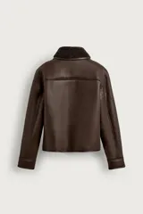Campera estilo cazadora color marrón de corte cropped, confeccionada en tejido efecto piel con interior de borreguillo a tono. Cuenta con cuello solapa, manga larga, bolsillos de plastrón en el pecho con solapa y botones, bolsillos de vivo en la cadera y cierre frontal de botonadura.
