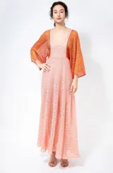 Vestido largo de tejido calado color salmón con diseño geométrico y escote en V. Se combina con una capa o bolero de manga ancha en tono naranja.
