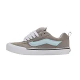 Championes Vans modelo Knu Skool, de diseño robusto y acolchado. Presentan una capellada de gamuza en color gris con la icónica banda lateral Sidestripe en tono celeste claro. Cuentan con cordones gruesos blancos, lengüeta y cuello acolchados, y suela de goma blanca con la clásica banda negra.