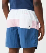 Bermuda de baño para hombre, color azul con recortes en bloques de color (azul más claro y rosa pálido). Presenta cintura elástica con cordón de ajuste y es de tejido plano de poliamida.