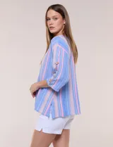 Blusa Erika de algodón con estampado de rayas en tonos azules, rosados y amarillos. Presenta cuello redondo con escote en V y botones frontales, mangas cortas decoradas con una fila de botones en los laterales y dobladillo asimétrico.