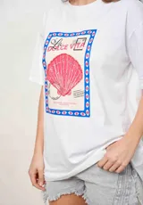 Remeron blanco de algodón, de corte oversize, con mangas cortas y estampa frontal estilo postal con una concha marina rosa y la inscripción 'La Dolce Vita'.