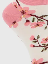 Calcetín corto de algodón con diseño estampado de ramas con flores de cerezo en tonos rosados sobre fondo crema. Presenta borde superior con terminación ondulada y puntera y talón reforzados en color rosa.