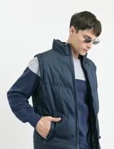 Chaleco capitoneado de color azul marino con cierre frontal completo y cuello alto. Presenta un diseño acolchado con costuras horizontales y forro interior con estampado escocés.