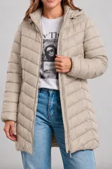 Campera puffer larga color beige, con diseño acolchado de líneas horizontales y diagonales, cierre frontal completo y capucha integrada.