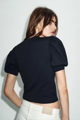 Jersey de punto negro con cuello redondo y mangas cortas abullonadas. Presenta una abertura frontal en forma de corazón.