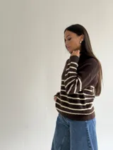 Sweater de punto a rayas horizontales en color marrón y crema, con cuello alto y cierre frontal parcial. Presenta un diseño de manga larga con detalles de hilo brillante en las rayas claras.
