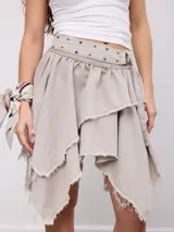 Falda midi asimétrica de denim color gris claro, con volados escalonados de bordes deshilachados y cintura con trabillas, tachas metálicas y cinturón integrado con hebilla.