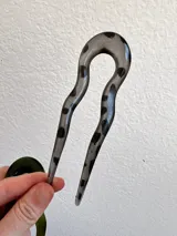 Pinza para el pelo tipo peineta, con forma irregular y diseño en tonos grises y negros, hecha de acrílico.