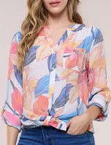 Blusa estampada Zac & Rachel con diseño floral en tonos rosados, azules y amarillos sobre base blanca. Presenta escote en V con botones frontales, mangas tres cuartos con presilla para arremangar y detalle de nudo en el ruedo.