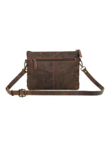 Cartera tipo bandolera de color marrón con diseño que combina dos texturas, presentando una parte superior de cuero liso y una inferior con acabado de pelo. Cuenta con costuras decorativas tipo festón en la unión de los materiales, cierre superior de cremallera y correa larga ajustable.