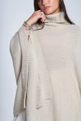 Poncho tejido color beige, con cuello alto y corte asimétrico.