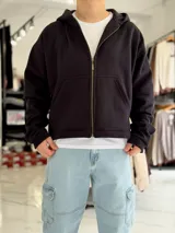 Campera negra de corte boxy fit con capucha, cierre frontal metálico y bolsillos tipo canguro.