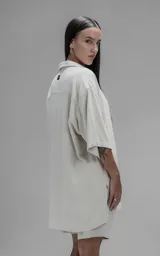 Camisa de corte oversize con cuello camisero, cierre frontal de botones y mangas cortas. Presenta un diseño holgado con bolsillos laterales integrados en la costura.