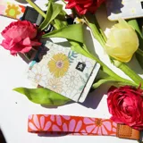 Billetera elástica con estampado de flores en tonos beige, amarillo y verde.