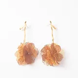 Caravanas colgantes con diseño de flor tridimensional, combinando pétalos de malla metálica dorada y tela semitransparente en tono marrón. Presentan un tallo largo y estilizado en metal dorado con cierre de perno.