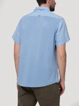 Camisa de manga corta RKF modelo Linenpro, color celeste, confeccionada en lino 100% orgánico, con cuello abierto, cierre frontal de botones y un bolsillo aplicado en el pecho.