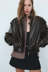 Cazadora de cuero sintético con cuello subido, manga larga con puños y trabillas en los hombros. Presenta un diseño abullonado en la cintura, bolsillos laterales y cierre frontal con cremallera y botones a presión ocultos. Posee un acabado efecto lavado y forro interior a tono.