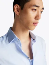 Camisa de algodón elástico color celeste, con microestampado integral de cuadros, cuello inglés y puños en inglete con dos botones. Cuenta con Flex Technology para mayor libertad de movimiento y logo de Tommy Hilfiger bordado en la manga.