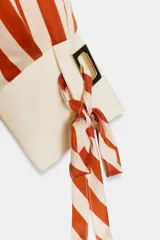 Camisa de manga larga con estampado de rayas verticales en color naranja y crema. Presenta cuello solapa, cierre frontal con botones dorados y puños anchos en color crema con detalle de lazos ajustables.