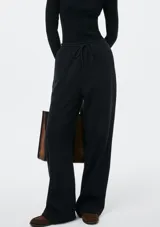 Pantalón de corte recto y holgado, color blanco, con cintura elástica y cordón ajustable. Presenta costuras verticales frontales que estilizan la silueta.