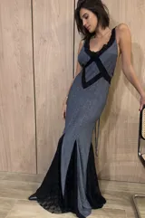 Vestido largo de silueta fluida, entallado en el torso, con escote profundo en V y espalda descubierta con tiras cruzadas. El cuerpo del vestido es de tejido jersey con lurex azul, y la falda presenta paneles triangulares de encaje negro con diseño de lunares.