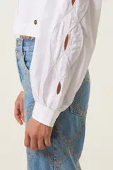 Camisa blanca corta de corte recto con cuello mao, mangas anchas con puños ajustados y aberturas trenzadas en las mangas. Incluye medalla de bronce con logo "TRS".