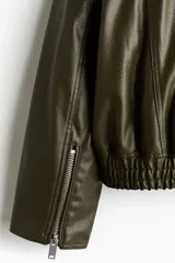 Cazadora estilo bomber en tejido revestido color verde militar, con cuello clásico, cierre frontal de cremallera metálica, bolsillos laterales y elástico fruncido en el bajo y los puños.