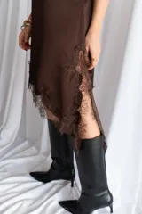 Vestido corto de satén negro, con tirantes finos, escote en V y detalles de encaje en el escote, el lateral y el dobladillo asimétrico.