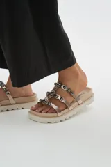 Sandalias chatas de plataforma dentada negra, con múltiples tiras metalizadas decoradas con tachas esféricas brillantes.