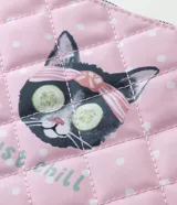 Neceser tipo sobre de color rosado con estampado de lunares blancos, ilustración de un gato con rodajas de pepino en los ojos y la frase "just chill". Cuenta con acabado acolchado matelaseado, volados de encaje blanco en los laterales y cierre superior con tirador en forma de corazón.