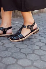 Sandalias de cuero negro con diseño de tiras entrecruzadas, hebilla dorada y suela plana.