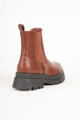 Botas Chelsea negras de cuero sintético con elástico en los laterales, detalle de textura símil cocodrilo en el talón y suela track.