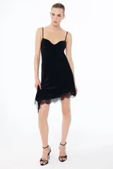 Vestido midi de terciopelo negro con escote en pico y tirantes finos ajustables. Presenta un diseño asimétrico en el bajo con aplicación de encaje a tono y espalda con tiras cruzadas.
