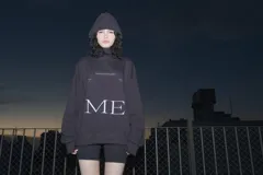 Hoodie negro oversize con capucha y cordón ajustable. Estampa frontal con la palabra "ME" en letras mayúsculas blancas.