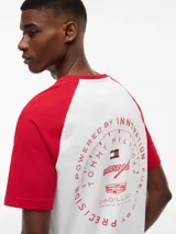 Remera de cuello redondo con diseño de mangas raglán en color rojo y cuerpo en color blanco. Presenta un estampado gráfico en el pecho con banderas de carreras y el logo de la colaboración Tommy Hilfiger x Cadillac Formula 1 Team.