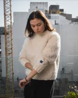 Sweater de cuello redondo tejido a mano en dos agujas, confeccionado en una mezcla de lana merino y seda. Presenta un diseño de punto grueso con detalle de bordado artesanal en color azul.