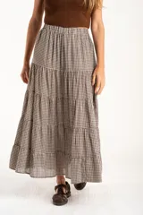 Falda larga de corte evasé con diseño de cuadros vichy en tonos marrón y blanco. Presenta una cintura elástica y un diseño de tres volados horizontales que aportan volumen y movimiento.