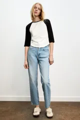 Jeans de mujer, tiro alto, color azul medio con efecto desgastado (lavado claro en muslos y oscuro en bordes). Corte recto y ancho (mom fit) con cinco bolsillos y cierre frontal de botón y cremallera.