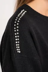 Sweater de lana color negro, de corte oversize, con cuello redondo, mangas largas y detalle de apliques metálicos en los hombros.
