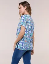 Blusa de manga corta con escote en V y pechera bordada. Presenta un estampado multicolor sobre base blanca, con pliegues frontales y aberturas laterales en el ruedo.